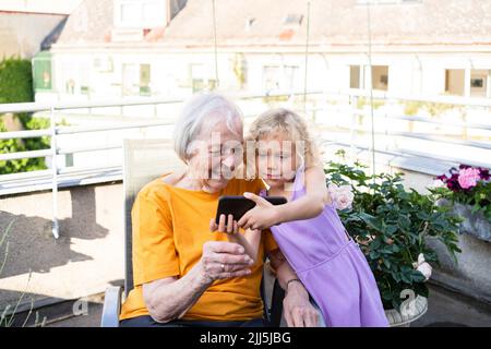 Granddaughter showing mobile phone to grandmother in balcony Stock Photo