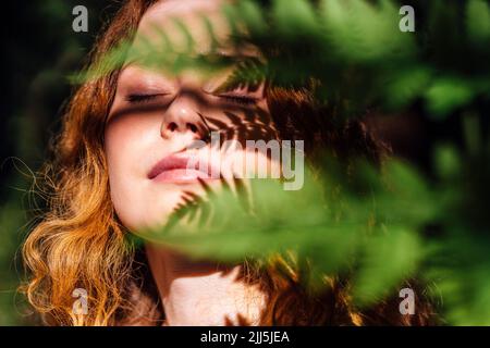 Woman with leaf shadow on face enjoying sunlight Stock Photo