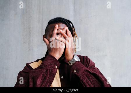 Man covering face with hands in front of wall Stock Photo