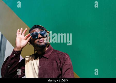 Man looking up wearing sunglasses by green wall Stock Photo