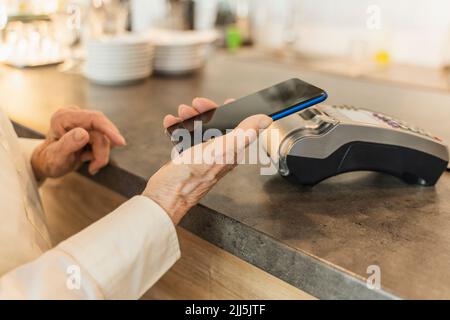Senior woman paying through mobile phone at cafe Stock Photo