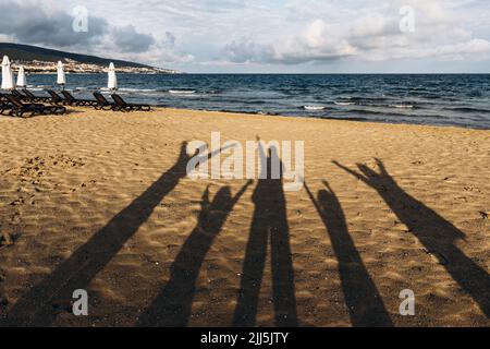 Shadows of five people standing on sandy beach with raised arms Stock Photo