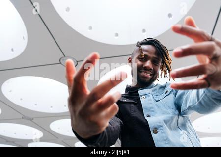 Smiling man with dreadlocks gesturing under illuminated ceiling Stock Photo