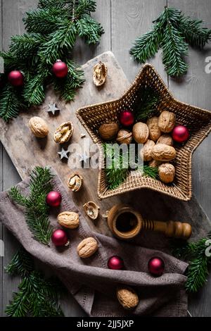 Studio shot of cutting board, star shaped wicker basket, twigs, Christmas ornaments, walnuts and simple nutcracker Stock Photo
