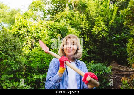 Smiling woman carrying shovel in garden Stock Photo