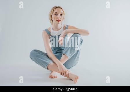 Young woman wearing overalls sitting against white background Stock Photo