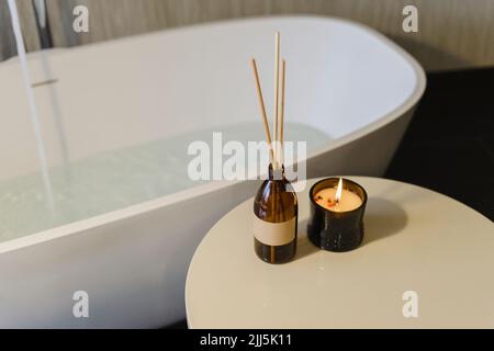 Incense sticks by burning scented candle on table near bathtub Stock Photo