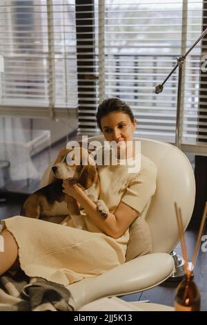 Thoughtful woman with dog sitting on couch at home Stock Photo