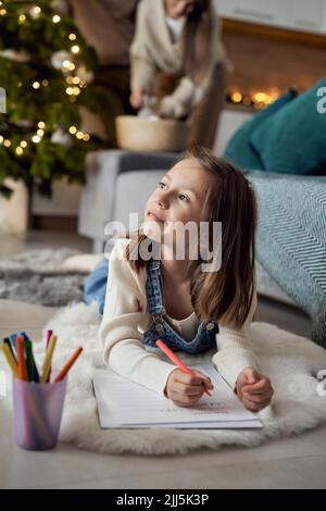Thoughtful girl writing letter to Santa Claus with parents in background at home Stock Photo