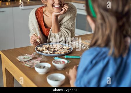 Happy mother with daughter decorating gingerbread cookie in kitchen Stock Photo