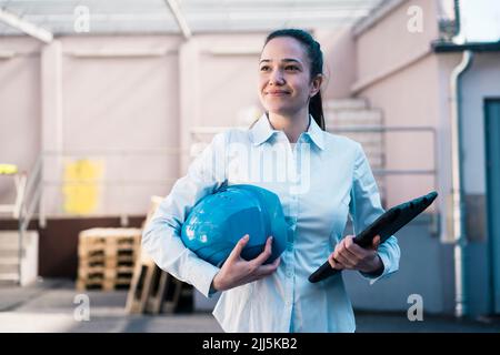 Smiling female architect with work helmet and tablet PC in industry Stock Photo