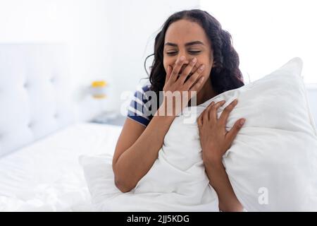 Young woman sitting and yawning on bed at home Stock Photo