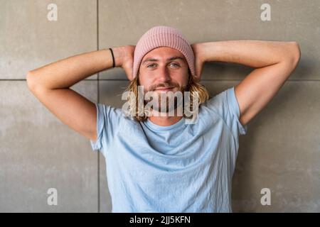 Smiling man with hands behind head in front of wall Stock Photo