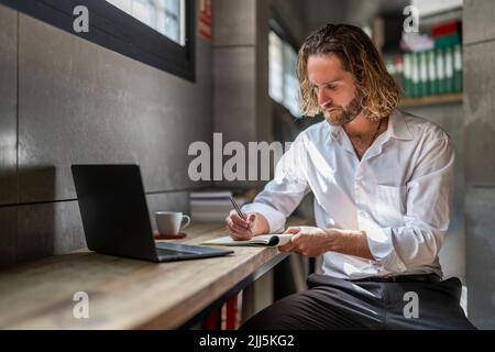 Executive writing in diary sitting with laptop on table at office Stock Photo