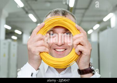 Smiling businessman looking through rolled up yellow cable at industry Stock Photo