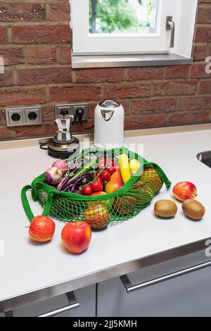 Fresh fruits and vegetables in reusable shopping bag on kitchen counter at home Stock Photo