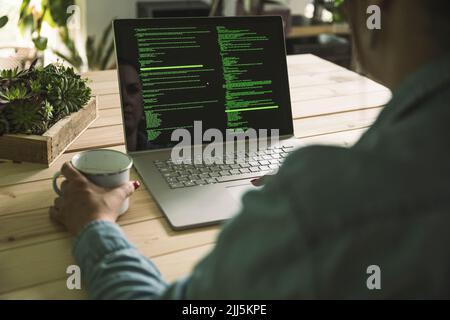 Hand of freelance computer programmer holding coffee cup at table working in home office Stock Photo
