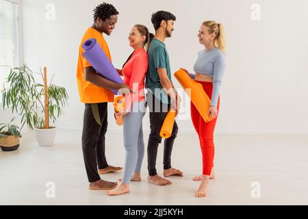 Men and women holding exercise mats talking with each other at yoga class Stock Photo