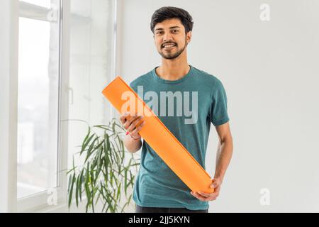 Smiling young man holding exercise mat in yoga studio Stock Photo
