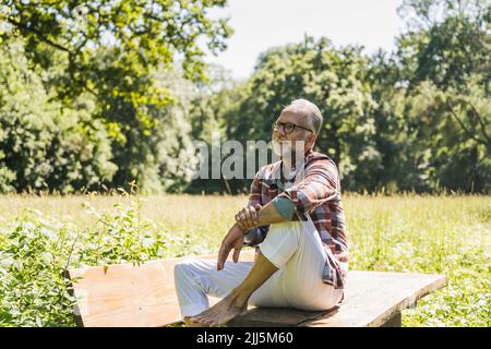 Smiling senior man wearing eyeglasses sitting on picnic table Stock Photo
