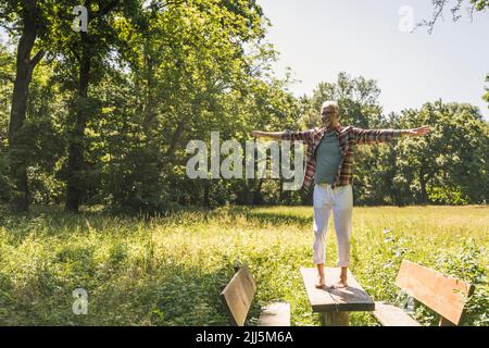 Happy man with arms outstretched standing on picnic table Stock Photo