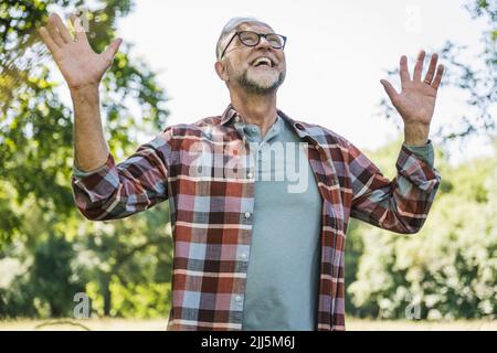 Cheerful senior man with arms raised standing in park Stock Photo