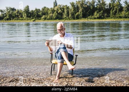 Smiling man using tablet PC sitting on chair at beach Stock Photo