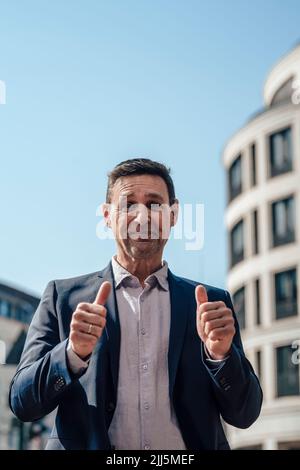 Smiling mature businessman showing thumbs up on sunny day Stock Photo