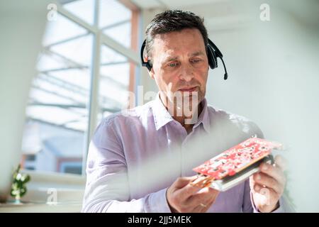 Working man wearing headset analyzing machine part at office Stock Photo
