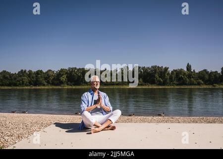 Senior man practicing yoga at riverbank on sunny day Stock Photo