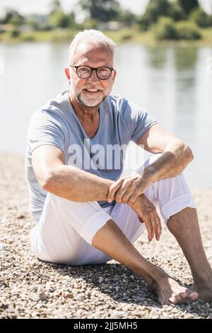 Smiling man wearing eyeglasses sitting at riverbank Stock Photo