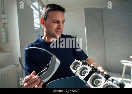 Smiling engineer holding virtual reality headset looking at lighting equipment at office Stock Photo