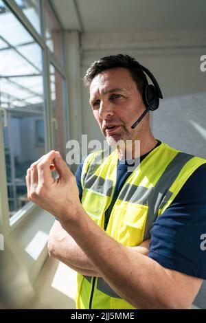 Engineer wearing reflective clothing talking on headset at office Stock Photo