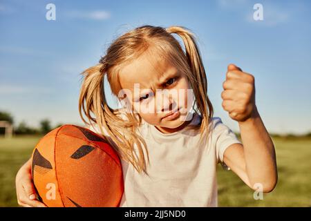 Blond girl holding rugby ball gesturing fist on sunny day Stock Photo