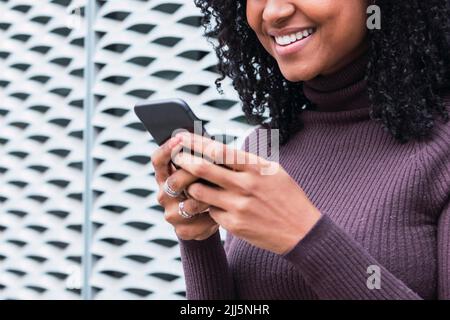 Happy woman surfing net through mobile phone in front of wall Stock Photo