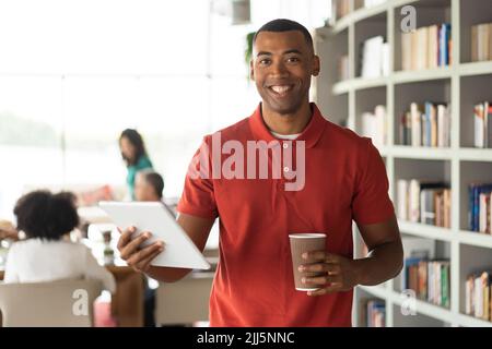 Smiling businessman holding disposable cup and tablet PC standing at office Stock Photo