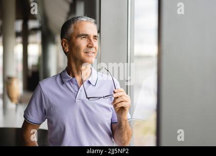 Businessman holding eyeglasses looking out of window at office Stock Photo