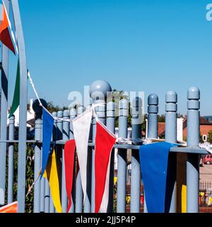 Dorking Surrey Hills UK, July 08 2022, Colouful Bunting Flags Hanging From A Blue Painted Metal Fence Against A Blue Sky With No People Stock Photo
