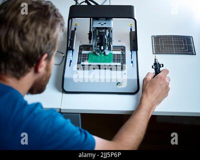 Technician looking at milling machine cutting circuit board in electronic laboratory Stock Photo