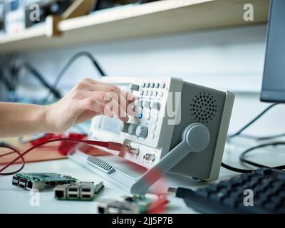 Hand of technician adjusting oscilloscope in electronic laboratory Stock Photo