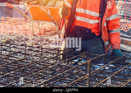 Builder's hands fixing steel reinforcement bars at construction site. Steel fixer assembling reinforcement cage. Selective focus Stock Photo