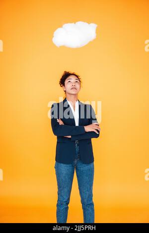 Businesswoman looking at cloud levitating over her against yellow background Stock Photo