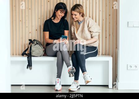 Smiling woman showing smart phone to friend after yoga session in health club Stock Photo