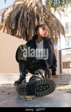 Contemplative young woman in jacket sitting on walkway Stock Photo
