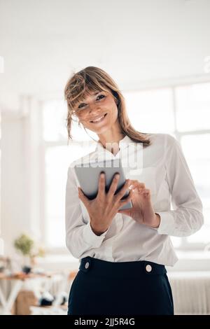 Smiling businesswoman with tablet PC standing in office Stock Photo