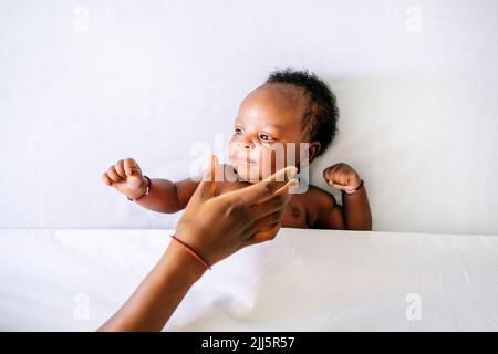 Hand of mother reaching baby boy lying on bed at home Stock Photo