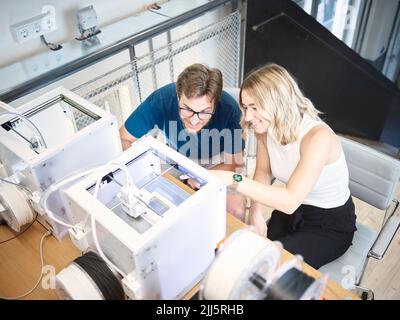 Smiling engineers discussing over 3d printer at workshop Stock Photo
