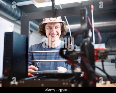 Smiling engineer looking at 3d printer at workshop Stock Photo