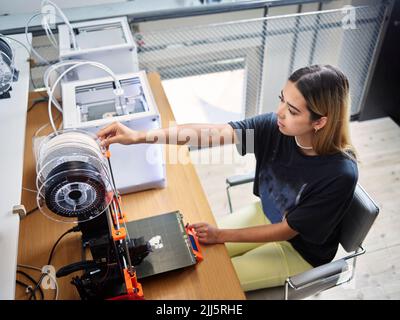 Young technician adjusting filament roll on 3d printer at workshop Stock Photo