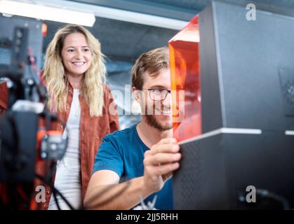 Smiling engineer assembling SLA printer with colleague at workshop Stock Photo